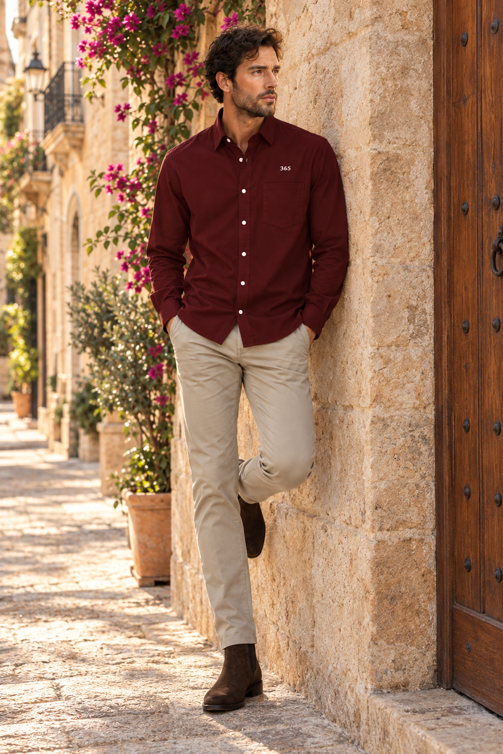 Camisa borgoña, apoyado en la fachada de piedra